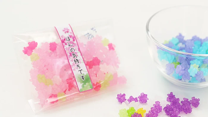 A small bag of konpeito sugar candy printed ほんの気持ちです, with loose candies and a glass bowl (seller photo).